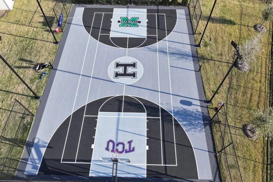 Aerial view of a custom-painted basketball court with team logos, fencing and lighting poles