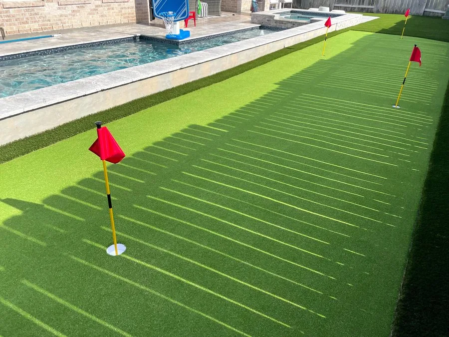Backyard artificial putting green with flags beside a pool