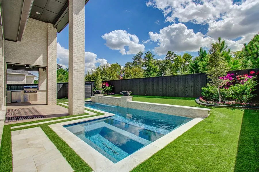 Backyard pool and spa surrounded by artificial turf lawn and stone pavers