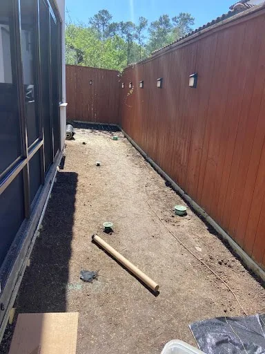 Bare graded soil with drain covers along a fenced side yard