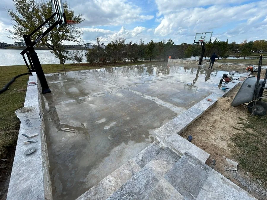 Concrete court slab being pressure washed beside a stone retaining wall and basketball hoop