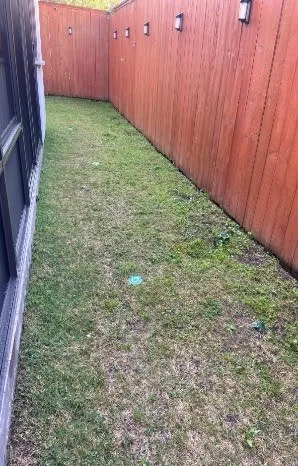 Existing side yard with patchy grass and bare spots before turf installation