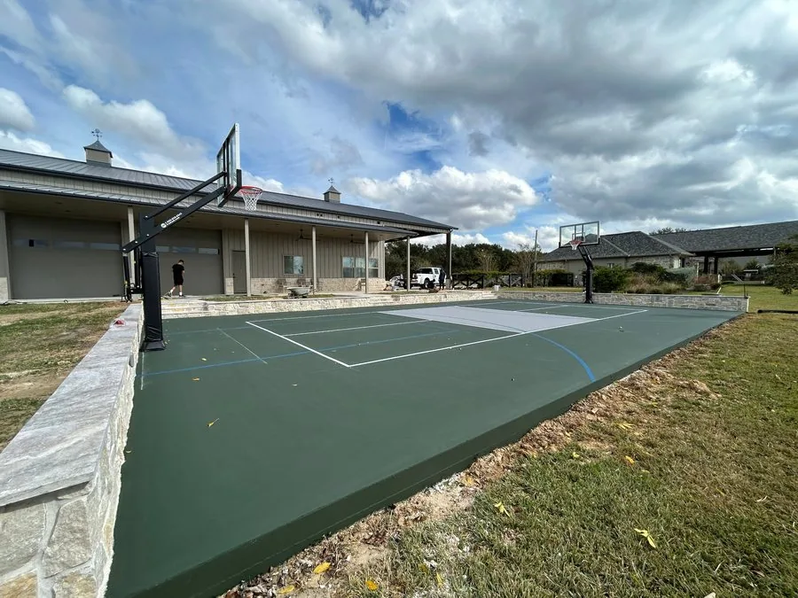 Finished dark green court with white lines, basketball hoops and a stone retaining wall