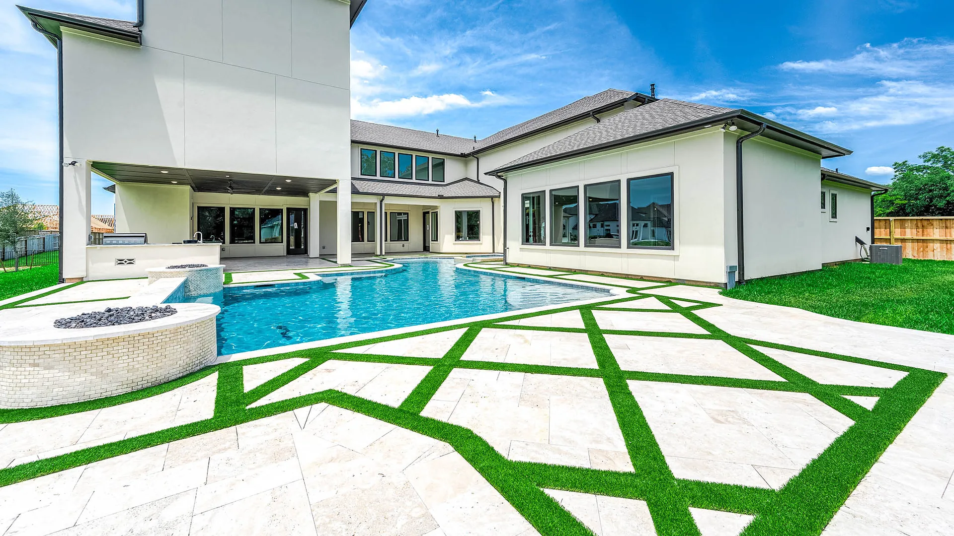 Pool deck with diagonal bands of artificial turf between travertine pavers behind a modern Houston home