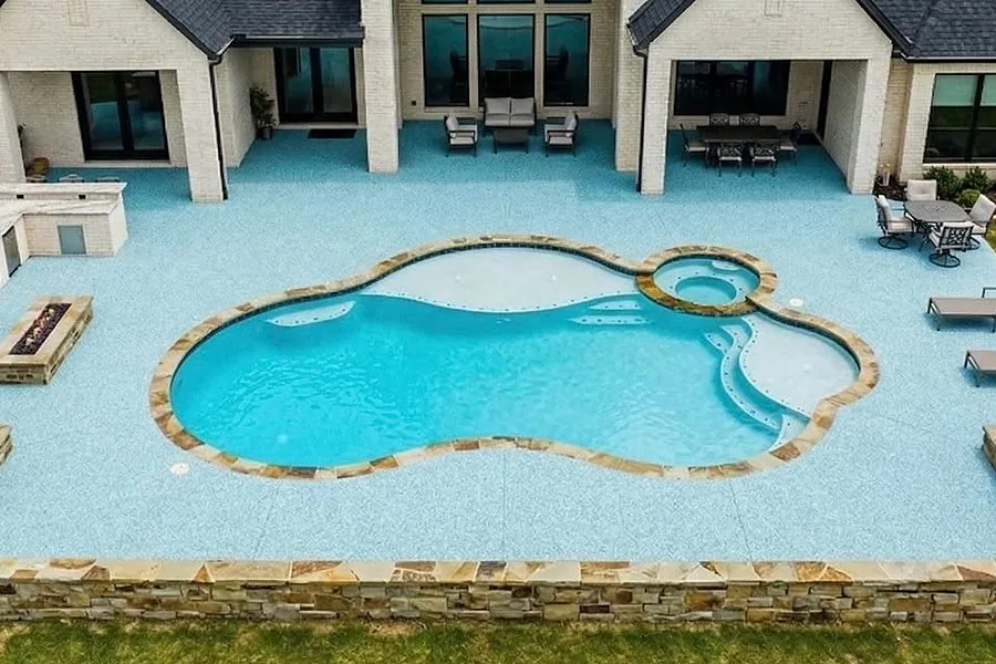 Pool surrounded by light blue poured rubber decking behind a large home