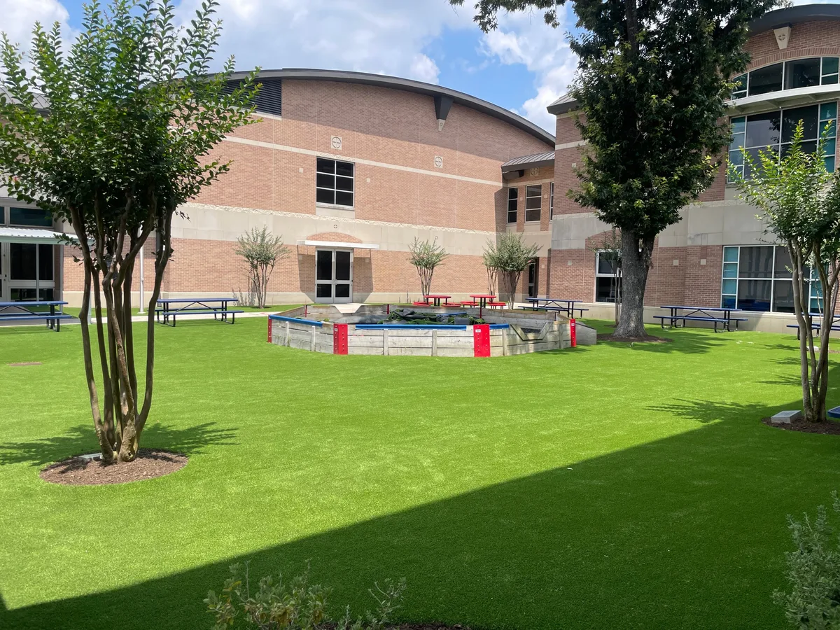 Artificial turf lawn in a school courtyard with trees and picnic tables